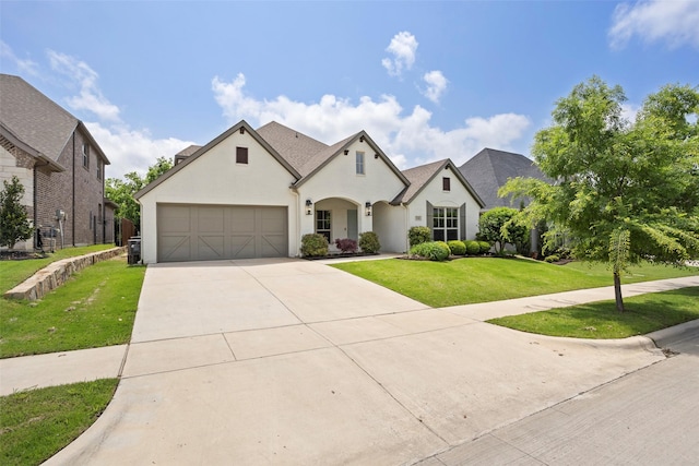french country style house featuring an attached garage, a front lawn, stucco siding, and driveway