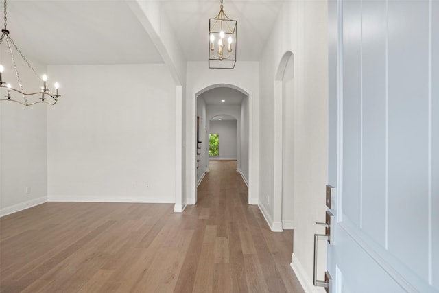 foyer entrance featuring arched walkways, baseboards, a notable chandelier, and light wood-style flooring