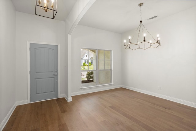 foyer entrance featuring visible vents, wood finished floors, baseboards, arched walkways, and a notable chandelier