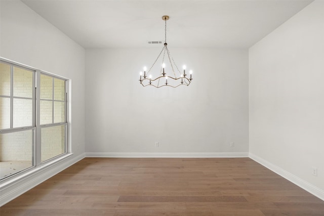 empty room with baseboards, an inviting chandelier, visible vents, and light wood-style floors