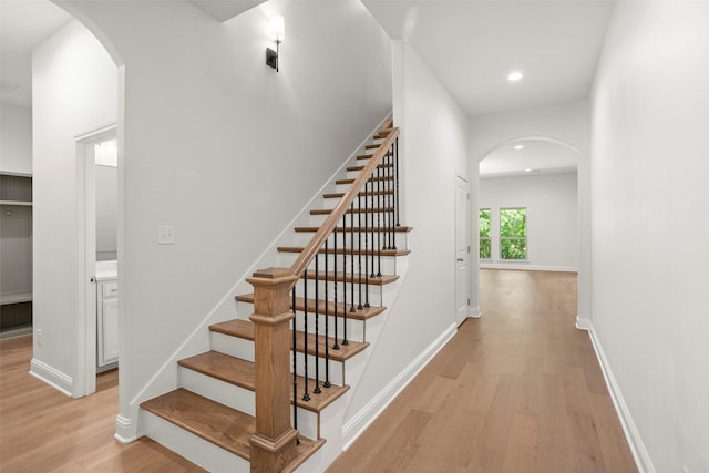 staircase with arched walkways, baseboards, recessed lighting, and wood finished floors