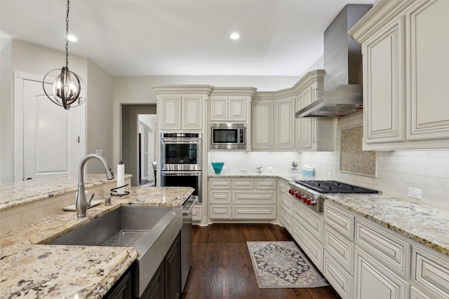 kitchen featuring wall chimney range hood, appliances with stainless steel finishes, cream cabinetry, a sink, and dark wood-type flooring