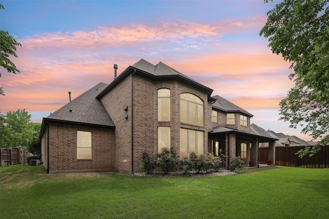 back of house featuring a yard, brick siding, fence, and roof with shingles