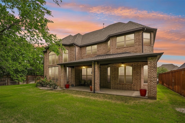 back of property at dusk with a patio, a yard, and brick siding