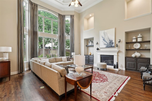 living room with ornamental molding, a towering ceiling, ceiling fan, dark wood-type flooring, and built in shelves