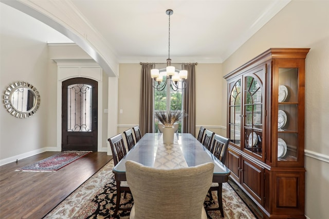 dining space with an inviting chandelier, arched walkways, baseboards, dark wood-type flooring, and ornamental molding