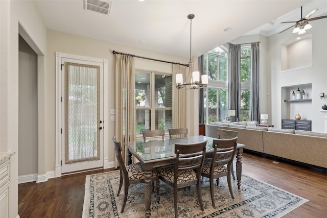 dining space featuring built in shelves, ceiling fan with notable chandelier, baseboards, dark wood-type flooring, and visible vents