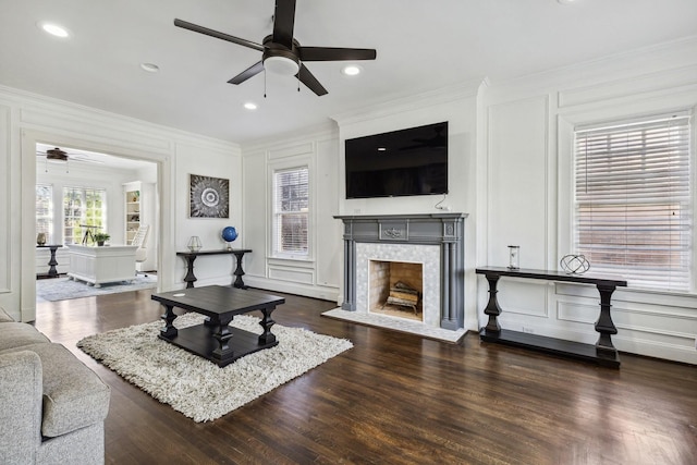 living area featuring crown molding, a ceiling fan, a decorative wall, and a tile fireplace