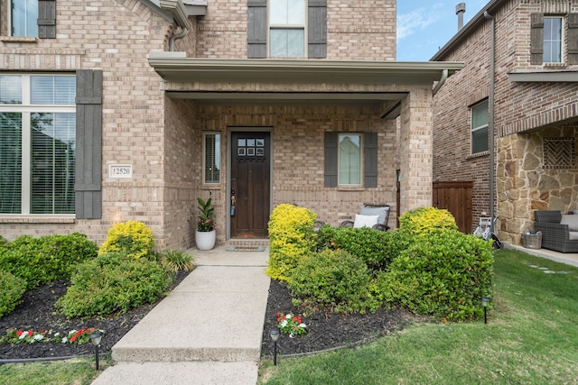 view of exterior entry with central air condition unit, brick siding, and a porch