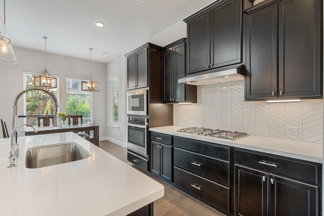 kitchen with a sink, light countertops, under cabinet range hood, stainless steel appliances, and dark wood-type flooring