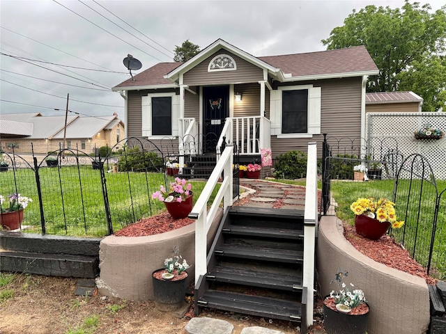 bungalow-style home with covered porch, roof with shingles, fence, and a front yard