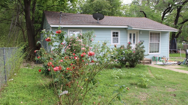 view of front facade featuring fence, roof with shingles, and a front lawn