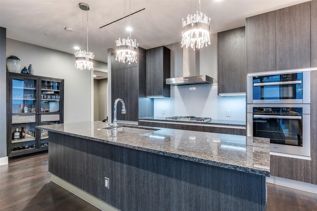 kitchen featuring an inviting chandelier, a spacious island, wall chimney range hood, a sink, and dark wood finished floors