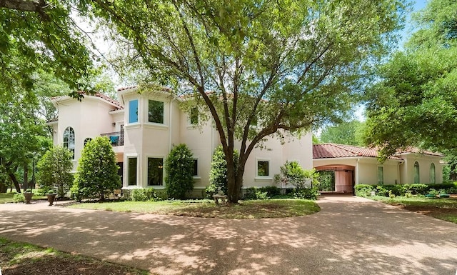 mediterranean / spanish-style home featuring curved driveway, stucco siding, and a tile roof