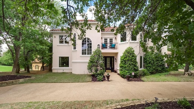 mediterranean / spanish-style house featuring french doors, a tile roof, a balcony, a front lawn, and stucco siding