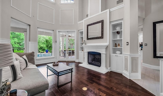 living area with wood finished floors, plenty of natural light, built in shelves, and a towering ceiling