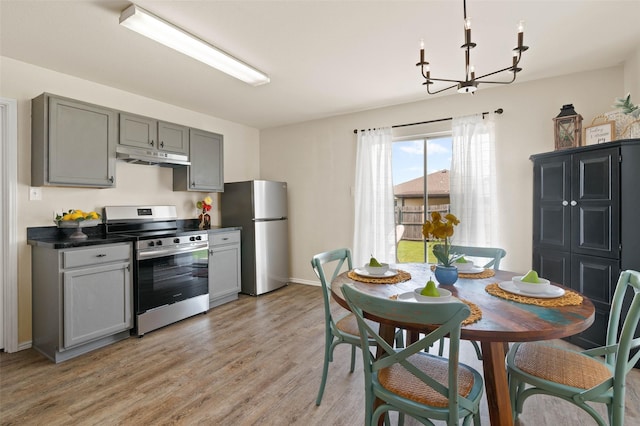 kitchen featuring gray cabinets, under cabinet range hood, a chandelier, light wood finished floors, and appliances with stainless steel finishes