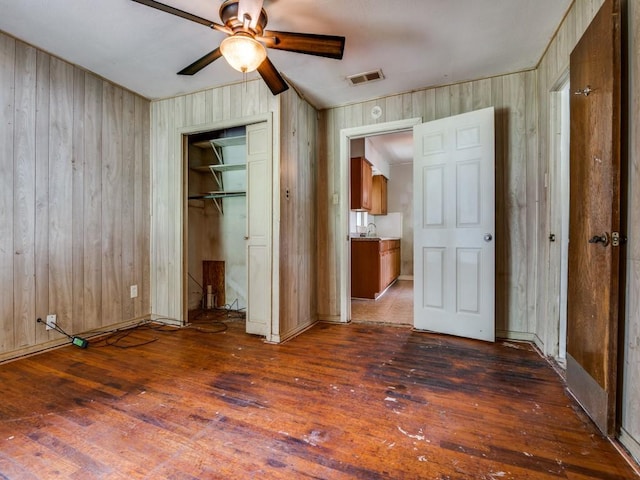 unfurnished bedroom with visible vents, a closet, wooden walls, hardwood / wood-style flooring, and a ceiling fan