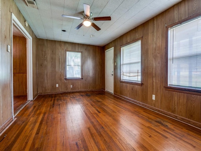 empty room with visible vents, a ceiling fan, wood-type flooring, and wood walls