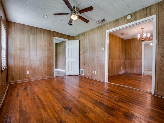 unfurnished room with visible vents, wood walls, ceiling fan with notable chandelier, and hardwood / wood-style floors