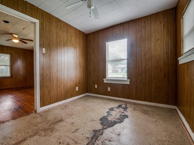 carpeted empty room featuring a ceiling fan and wooden walls