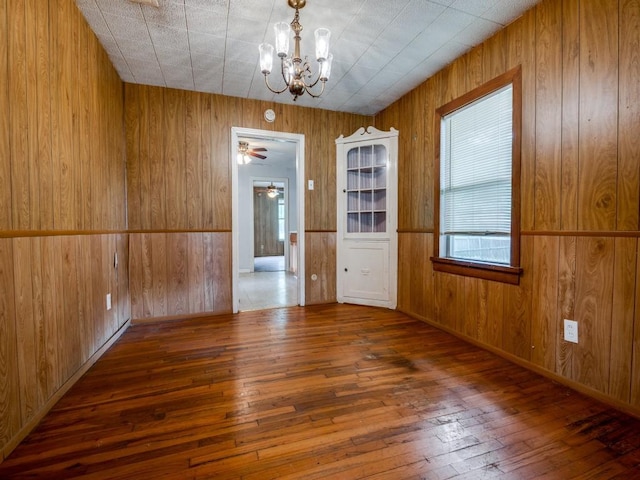 unfurnished dining area featuring wood walls, ceiling fan with notable chandelier, and hardwood / wood-style floors