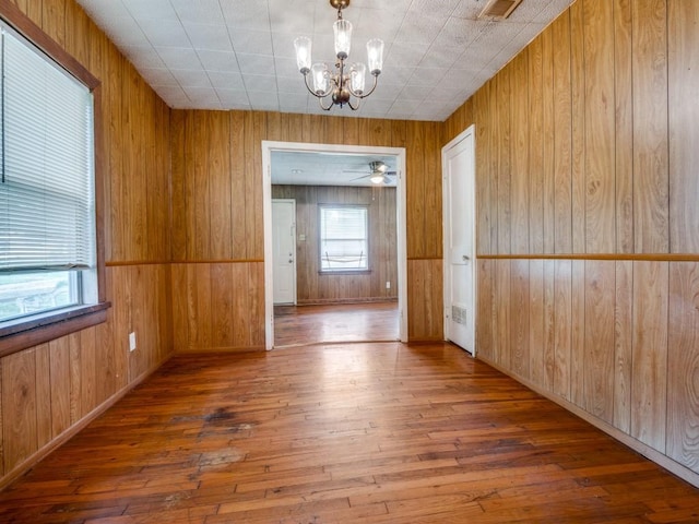 unfurnished dining area with an inviting chandelier, wooden walls, hardwood / wood-style floors, and visible vents