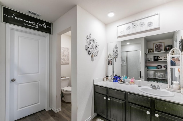 full bathroom featuring vanity, toilet, a shower stall, wood finished floors, and visible vents