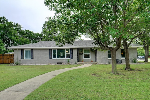 single story home featuring board and batten siding, a front yard, roof with shingles, brick siding, and fence
