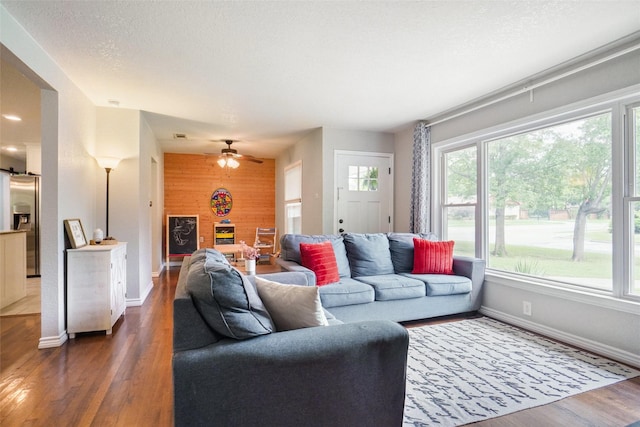 living room with baseboards, a ceiling fan, wood walls, and wood finished floors