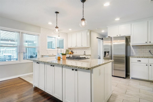 kitchen with backsplash, appliances with stainless steel finishes, a center island, light stone counters, and white cabinetry