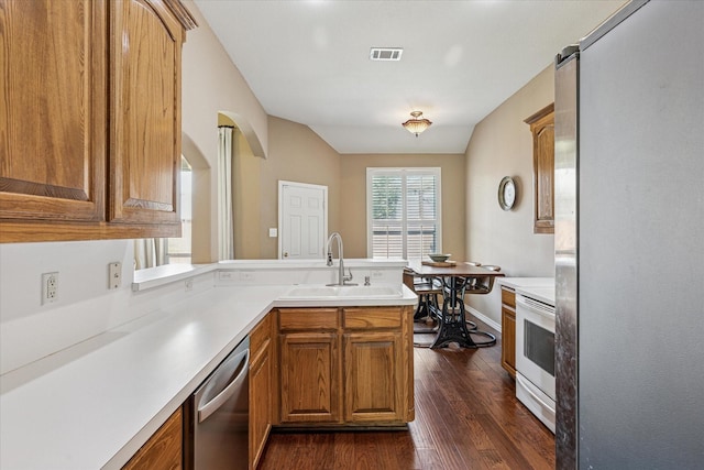 kitchen with appliances with stainless steel finishes, a sink, a peninsula, visible vents, and dark wood-style floors