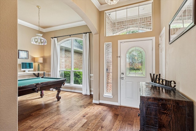 foyer entrance with crown molding, arched walkways, wood finished floors, and a chandelier