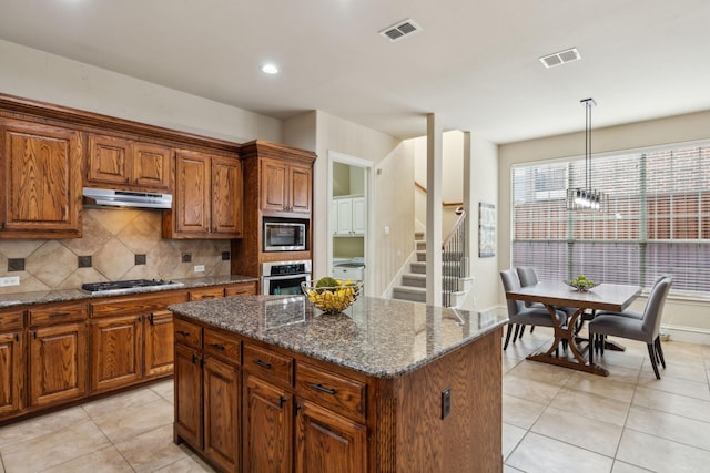 1016 Arches Park Dr, Allen, TX 75013 - kitchen featuring stainless steel appliances, under cabinet range hood, light tile patterned floors, backsplash, and dark stone countertops