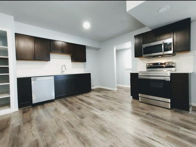 kitchen featuring appliances with stainless steel finishes, a sink, light wood finished floors, light countertops, and baseboards