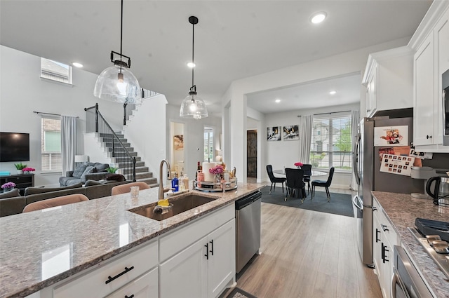 kitchen with white cabinets, a sink, light wood finished floors, dishwasher, and open floor plan