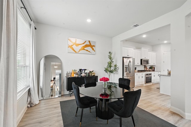 dining space featuring visible vents, light wood-style floors, baseboards, recessed lighting, and arched walkways