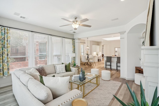 living area featuring visible vents, baseboards, ceiling fan, arched walkways, and light wood finished floors