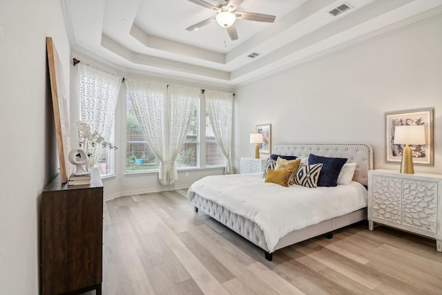 bedroom featuring a ceiling fan, a tray ceiling, visible vents, and light wood finished floors