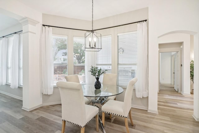dining space featuring baseboards, arched walkways, light wood finished floors, and a notable chandelier