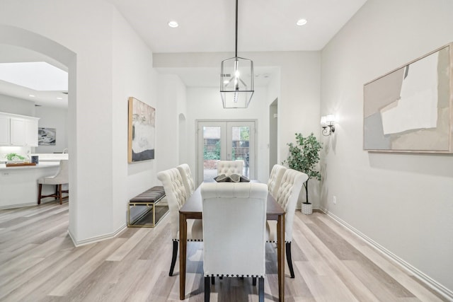 dining room featuring arched walkways, baseboards, french doors, and light wood-type flooring