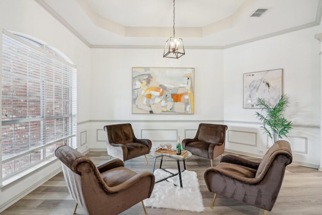 sitting room with an inviting chandelier, a raised ceiling, a decorative wall, light wood-style flooring, and visible vents