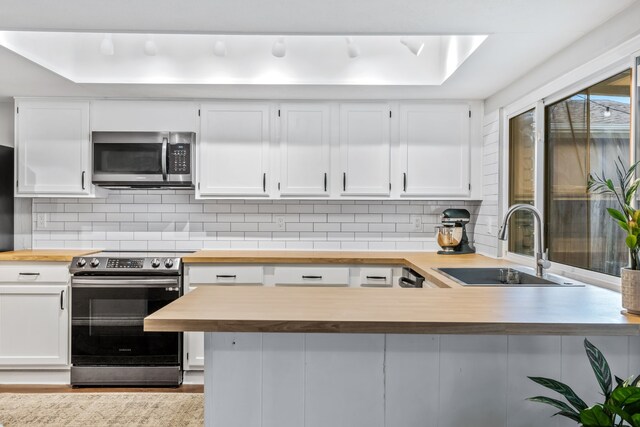kitchen with a sink, appliances with stainless steel finishes, white cabinetry, and wood counters