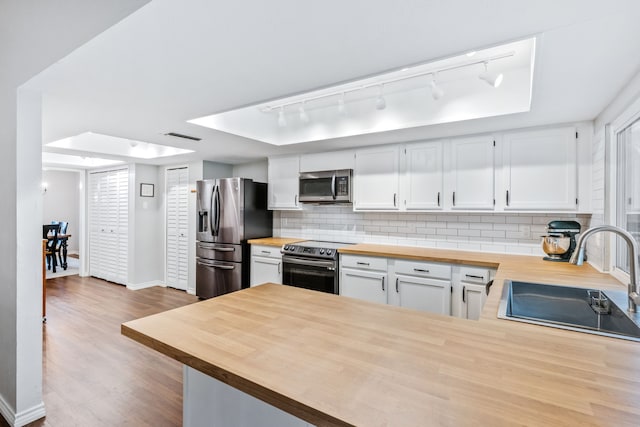 kitchen featuring track lighting, butcher block counters, a tray ceiling, a sink, and appliances with stainless steel finishes