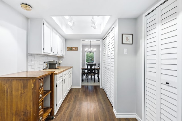 kitchen with white cabinets, a chandelier, baseboards, dark wood-type flooring, and butcher block counters