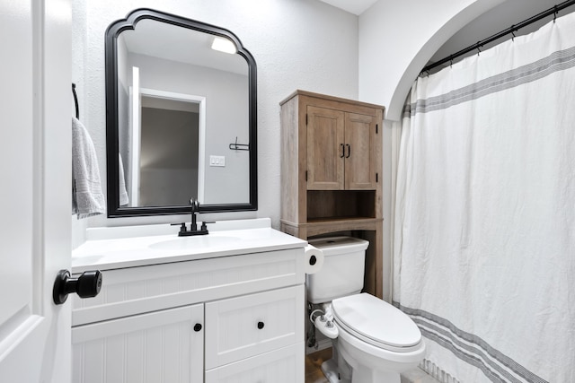 full bath with vanity, a textured wall, and toilet