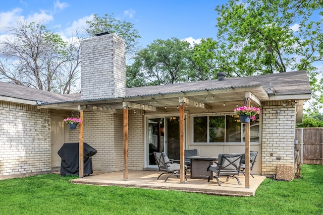 rear view of property featuring a chimney, a lawn, brick siding, fence, and a patio