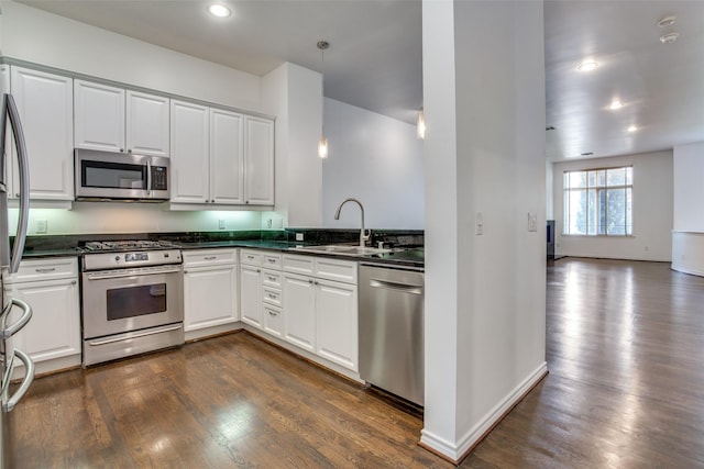 kitchen with dark countertops, a sink, stainless steel appliances, white cabinetry, and dark wood-style floors