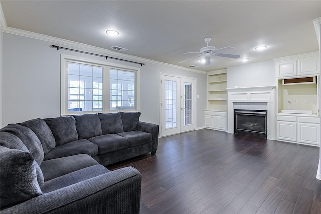 living area with visible vents, ornamental molding, a glass covered fireplace, ceiling fan, and dark wood-type flooring