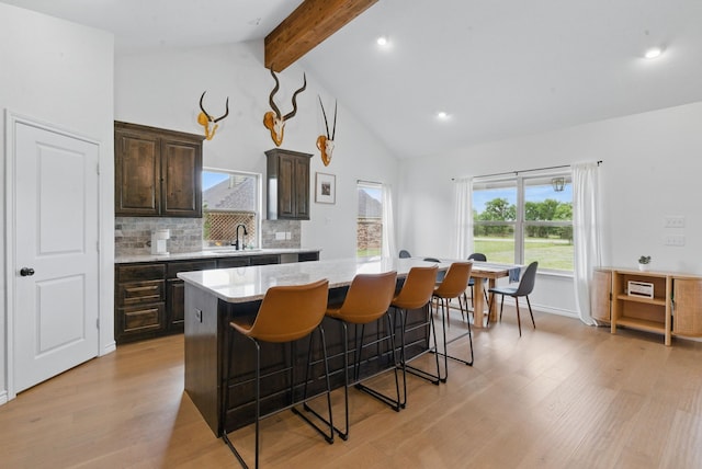 kitchen with dark brown cabinetry, light wood-style floors, a kitchen breakfast bar, a kitchen island, and beamed ceiling